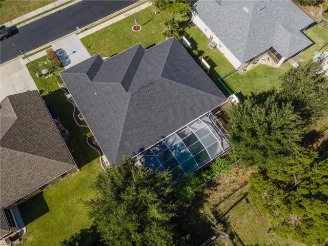 Overhead property view featuring a dark shingle roof, screened pool enclosure, and a manicured lawn