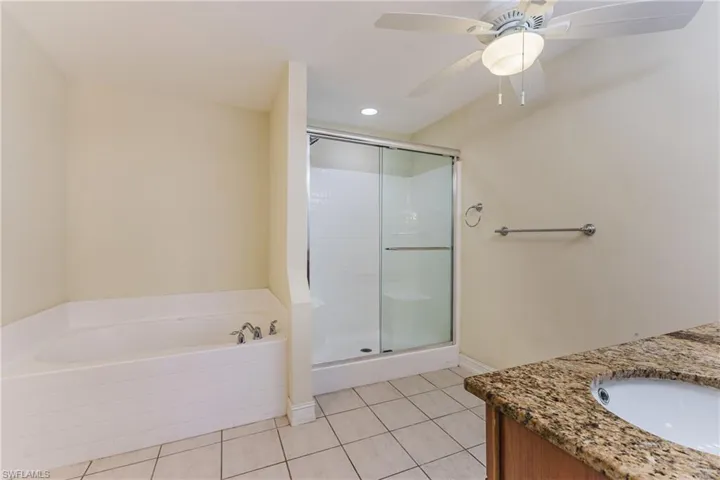 Bathroom featuring a built-in soaking tub, glass-enclosed shower, and a vanity with a stone countertop