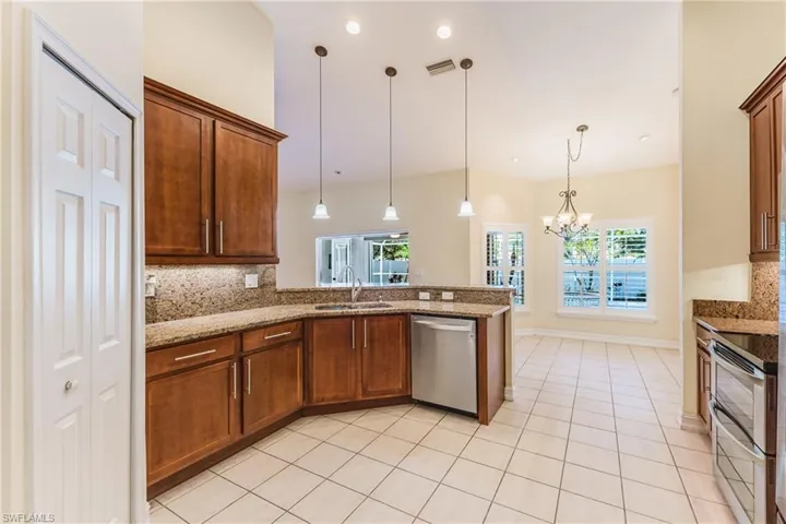 Kitchen featuring wood cabinetry, stone countertops, stainless steel appliances, tile flooring, and recessed lighting