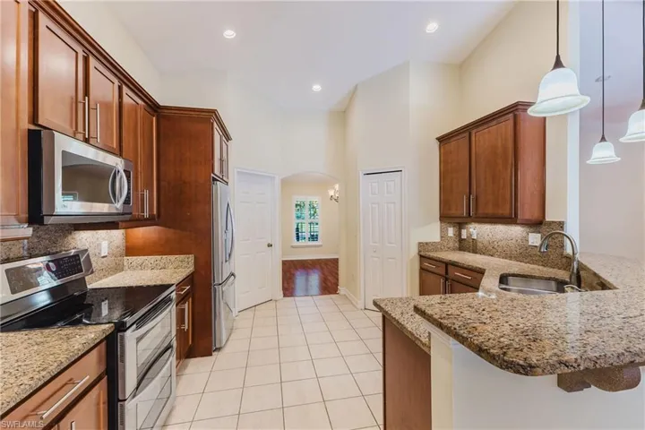 Kitchen featuring warm wood cabinetry, stainless steel appliances, speckled stone countertops, and tile flooring