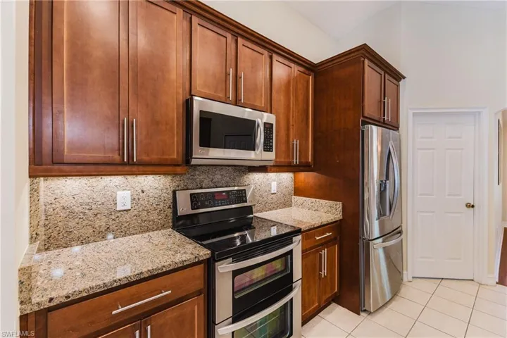 Kitchen featuring wood cabinetry, stainless steel appliances, granite countertops, tile flooring, and under-cabinet lighting