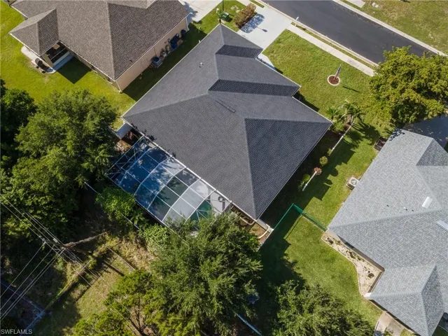 Aerial perspective of a single-story residence featuring a dark shingle roof and a screened-in pool enclosure