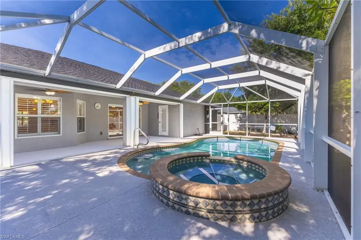 Screened swimming pool enclosure with integrated spa, concrete decking, and direct access to the interior via multiple sliding glass doors