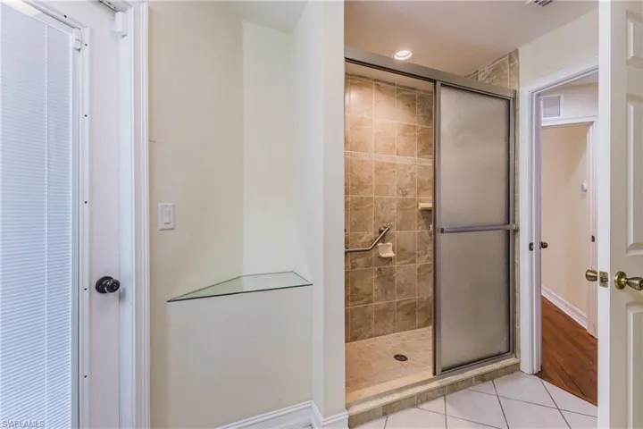 Walk-in shower with tiled walls and floor, featuring a sliding frosted glass door and grab bar