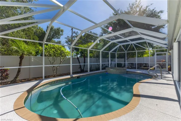 Screened enclosure featuring a freeform swimming pool with a mosaic tile spa, a non-slip textured deck, and integrated pool steps with a handrail