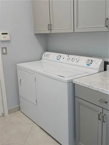 Laundry area featuring cabinets, light tile patterned flooring, and washing machine and clothes dryer