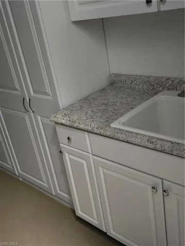 Details featuring white cabinetry, sink, and light stone counters