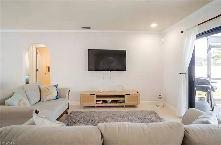 Carpeted living area featuring arched walkways, ornamental molding, and recessed lighting