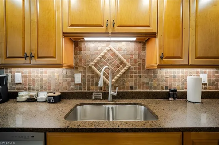 Kitchen featuring dark stone counters, backsplash, and dishwasher
