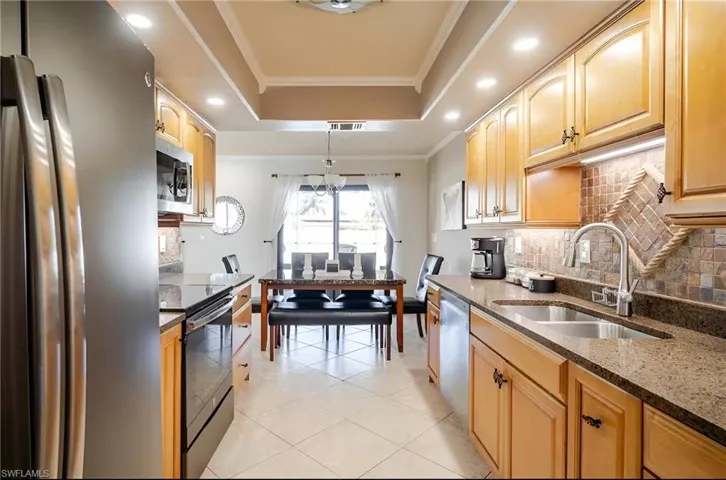 Kitchen featuring appliances with stainless steel finishes, crown molding, hanging light fixtures, dark stone counters, and recessed lighting