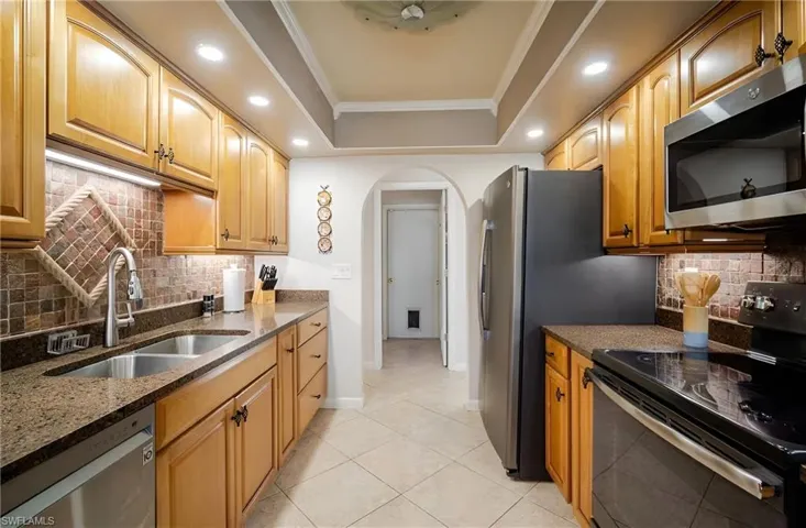 Kitchen with backsplash, appliances with stainless steel finishes, dark stone counters, a raised ceiling, and crown molding
