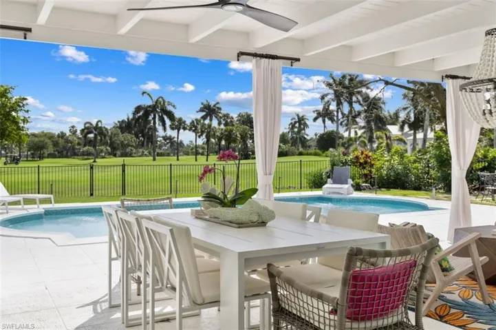 Fenced backyard with a patio, outdoor dining space, ceiling fan, and view of scattered trees