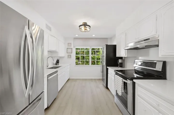 Kitchen featuring stainless steel appliances, white cabinetry, under cabinet range hood, recessed lighting, and light wood-type flooring