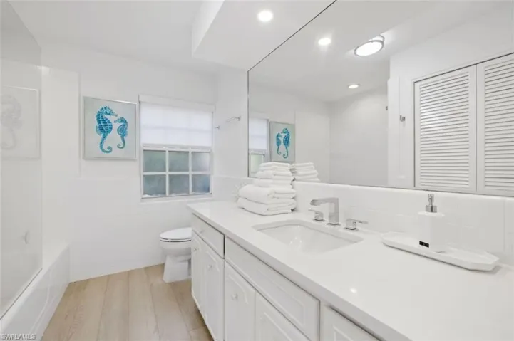 Full bath featuring vanity, light wood-style floors, tile walls, washtub / shower combination, and recessed lighting