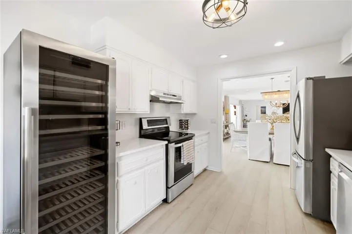 Kitchen with wine cooler, appliances with stainless steel finishes, light countertops, decorative light fixtures, and white cabinets