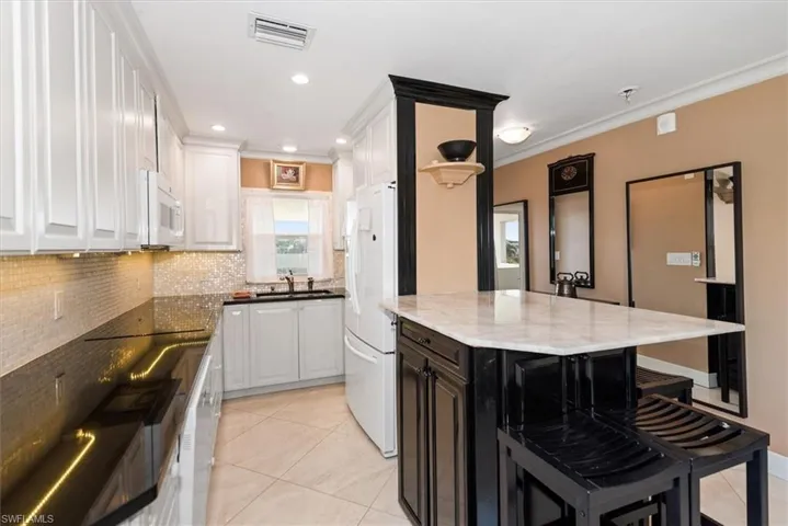 Kitchen with a breakfast bar, two tone cabinets, dark stone countertops, white appliances, and tasteful backsplash