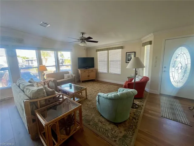 Living area featuring wood finished floors, healthy amount of natural light, ornamental molding, and ceiling fan
