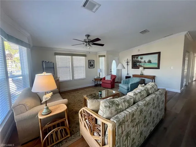 Living area featuring dark wood finished floors, ornamental molding, and ceiling fan