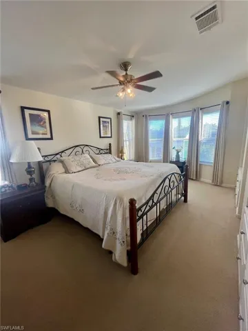 Carpeted bedroom featuring multiple windows and ceiling fan