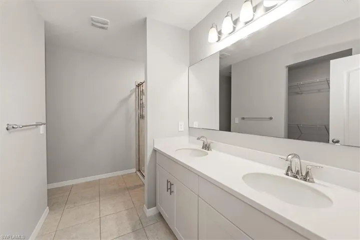 Full bathroom with double vanity, a stall shower, light tile patterned floors, and a spacious closet
