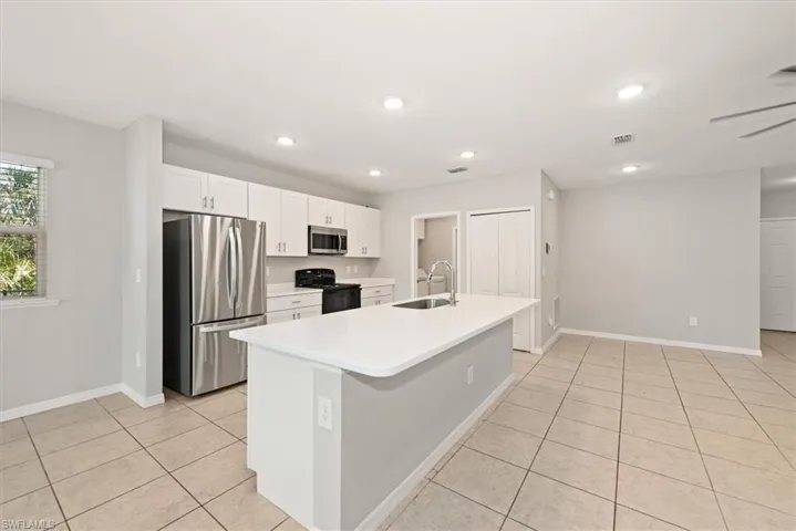 Kitchen with stainless steel appliances, white cabinets, a center island with sink, light tile patterned flooring, and recessed lighting