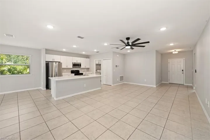 Kitchen with open floor plan, a kitchen island with sink, white cabinetry, stainless steel appliances, and a ceiling fan