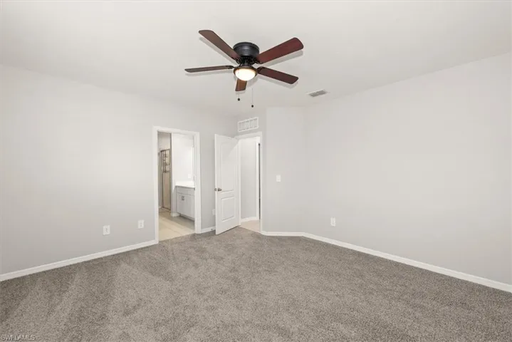 Unfurnished bedroom with light colored carpet, a ceiling fan, and connected bathroom