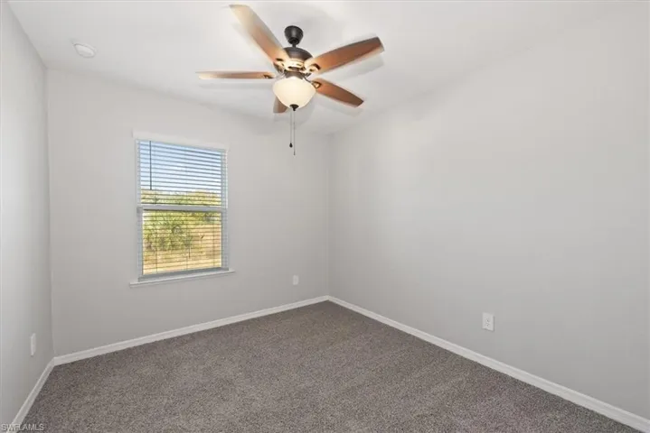Carpeted spare room with ceiling fan and baseboards