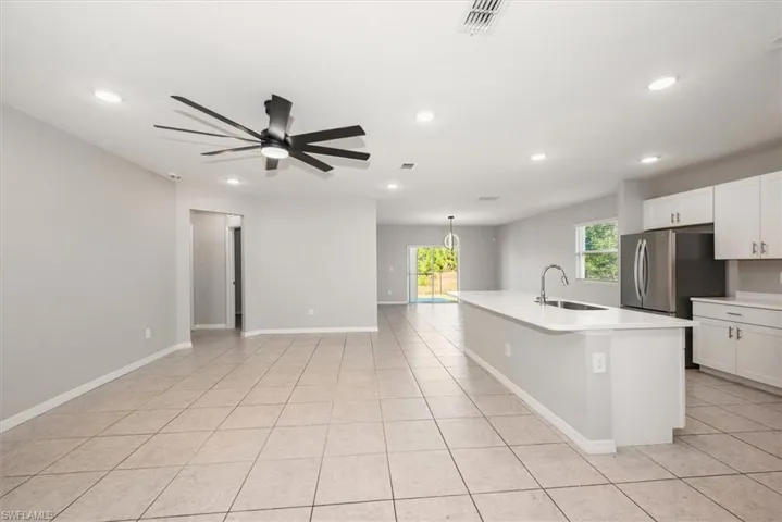 Kitchen with white cabinetry, an island with sink, hanging light fixtures, light tile patterned floors, and a chandelier