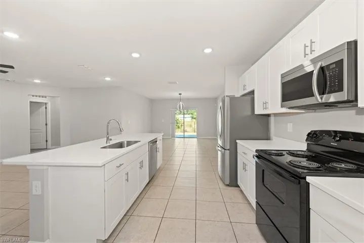 Kitchen featuring appliances with stainless steel finishes, white cabinetry, light tile patterned floors, a kitchen island with sink, and recessed lighting