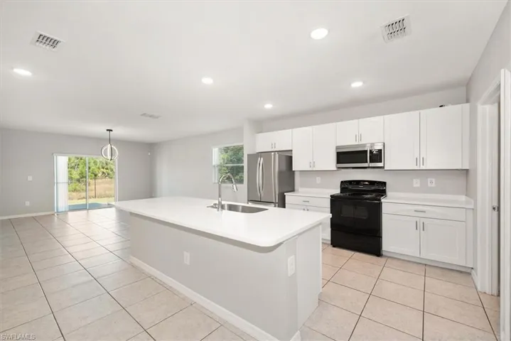 Kitchen with stainless steel appliances, light tile patterned flooring, white cabinets, a center island with sink, and recessed lighting