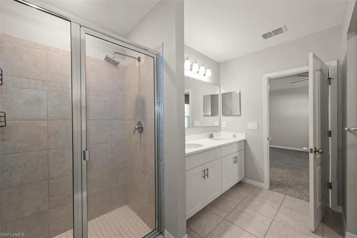 Bathroom featuring double vanity, light tile patterned floors, and a shower stall