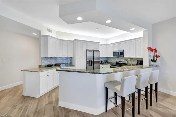Kitchen with stainless steel appliances, a peninsula, dark stone countertops, light wood-style flooring, and recessed lighting