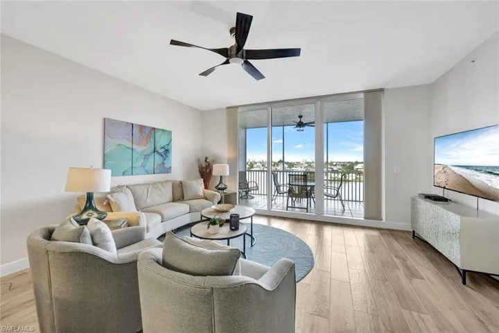 Living area with ceiling fan, light wood-style flooring, and a wall of windows