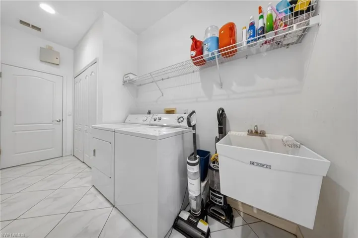 Laundry area featuring white tile flooring, a wall-mounted utility sink, and overhead wire shelving