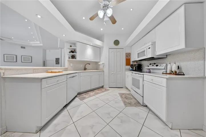 Contemporary kitchen featuring white cabinetry, light-toned countertops, and a white appliance suite