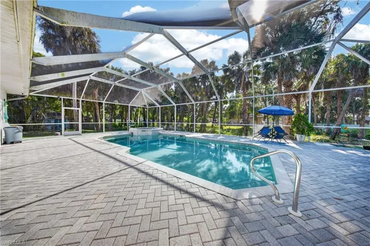 Screened pool enclosure featuring a rectangular pool with integrated spa and paver decking