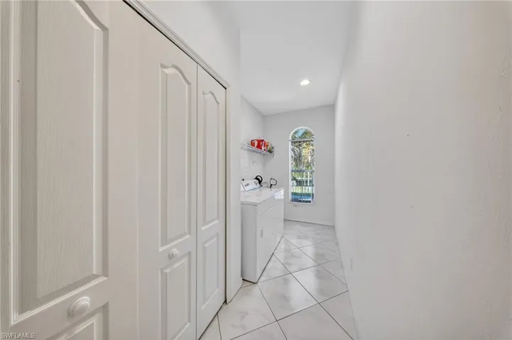 Dedicated laundry area featuring a white washer and dryer, tile flooring, an arched window, and built-in shelving