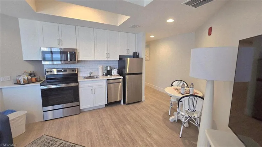 Kitchen featuring appliances with stainless steel finishes, decorative backsplash, white cabinets, light countertops, and light wood-style flooring