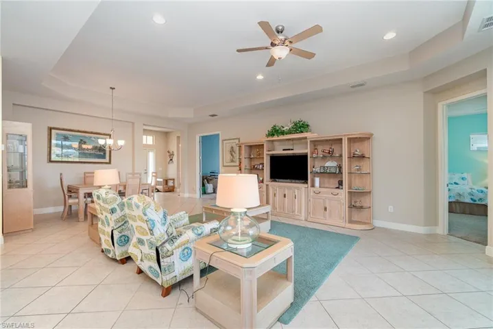 Living room with light tile floors, ceiling fan with notable chandelier, and a raised ceiling