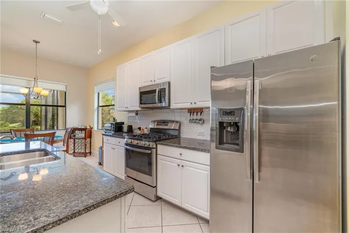 Kitchen featuring stainless steel appliances, backsplash, light tile floors, hanging light fixtures, and white cabinets