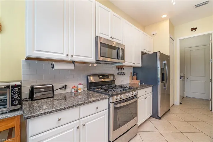 Kitchen featuring appliances with stainless steel finishes, white cabinetry, and backsplash