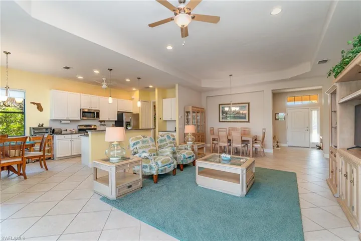 Living room featuring a raised ceiling, ceiling fan with notable chandelier, a healthy amount of sunlight, and light tile floors