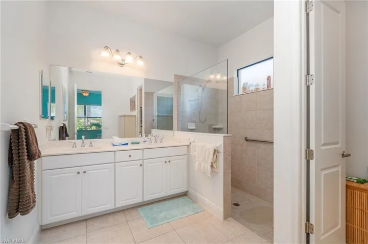 Bathroom featuring tiled shower, oversized vanity, double sink, and tile floors
