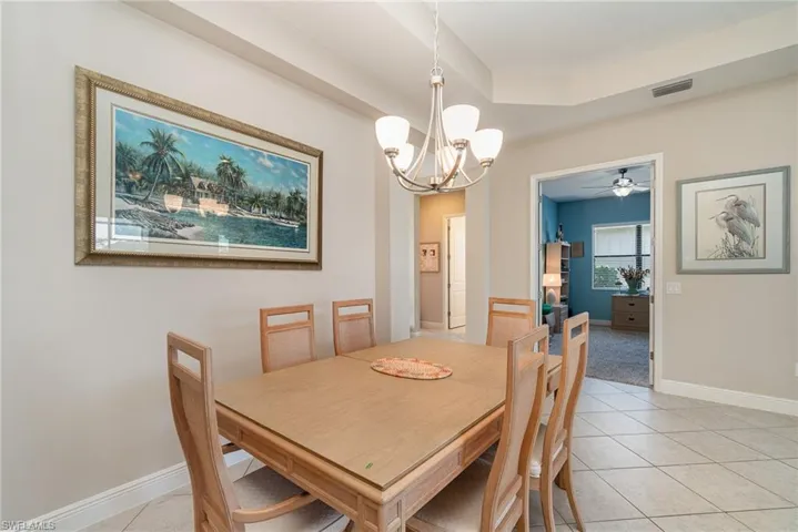 Tiled dining space featuring ceiling fan with notable chandelier and a tray ceiling