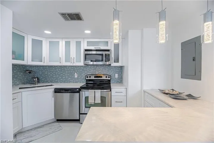 Kitchen featuring stainless steel appliances, glass insert cabinets, white cabinetry, electric panel, and pendant lighting