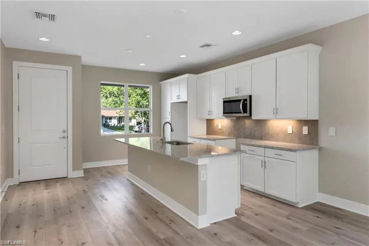 Kitchen with light hardwood / wood-style floors, sink, light stone counters, an island with sink, and white cabinets