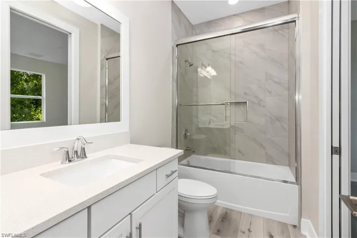 Full bathroom featuring toilet, vanity, hardwood / wood-style flooring, and enclosed tub / shower combo