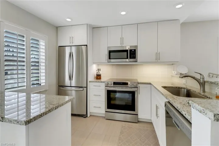Kitchen with light stone counters, appliances with stainless steel finishes, a peninsula, white cabinets, and recessed lighting