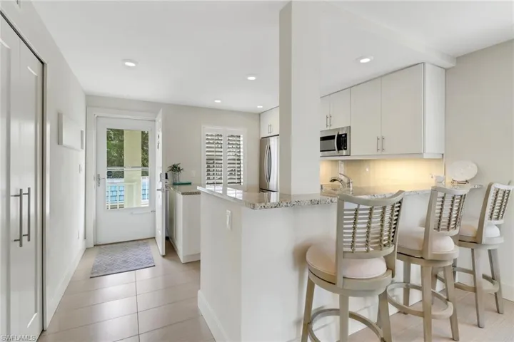 Kitchen featuring light stone counters, a breakfast bar, white cabinetry, decorative backsplash, and recessed lighting